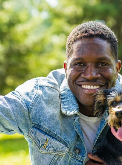latin american man taking selfie picture with his cute dog at sunny day in city park lawn on the grass.